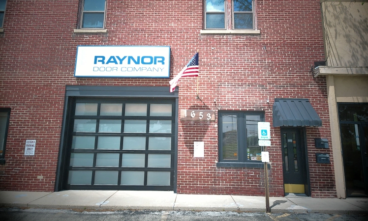 The Raynor Door Company brick building at 1653 Winnetka Avenue in Northfield, with the company sign and American flag.